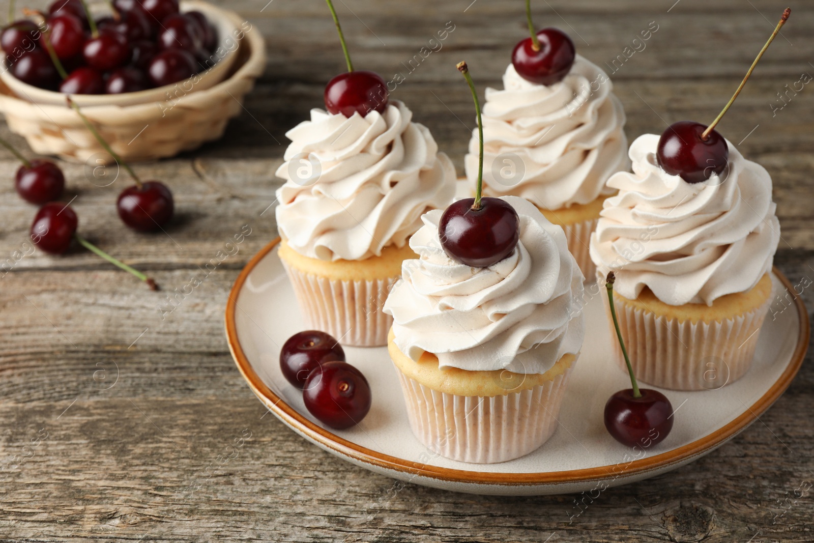 Photo of Delicious cupcakes with cream and cherries on wooden table, closeup