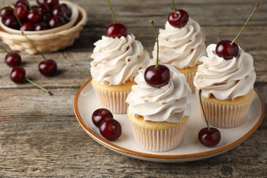 Photo of Delicious cupcakes with cream and cherries on wooden table, closeup