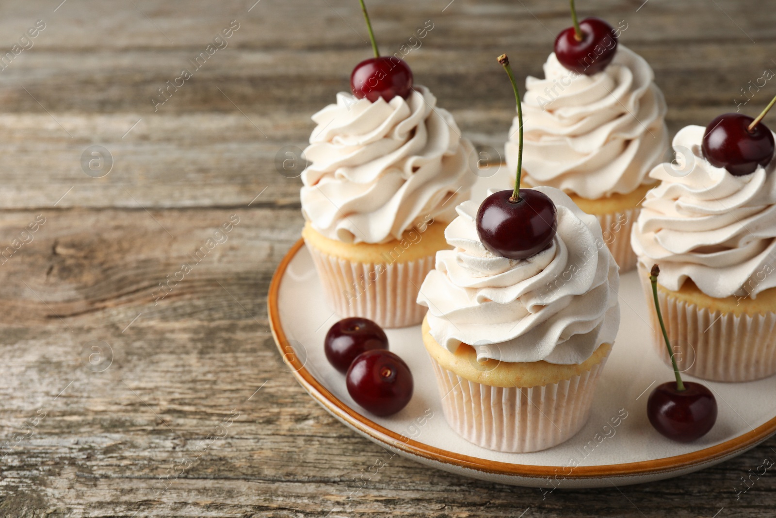 Photo of Delicious cupcakes with cream and cherries on wooden table, closeup. Space for text