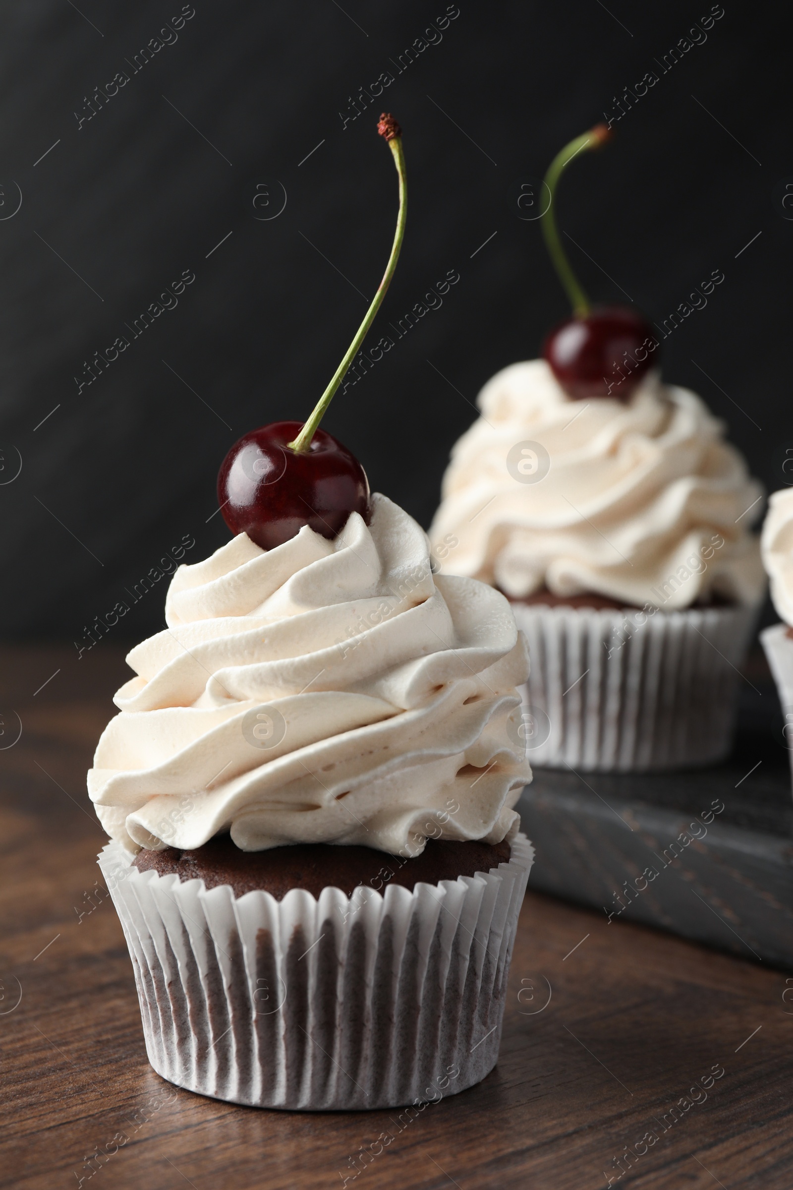 Photo of Delicious cupcakes with cream and cherries on wooden table, closeup