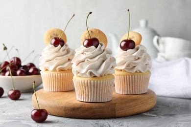 Photo of Delicious cupcakes with cherries and cookies on grey textured table, closeup