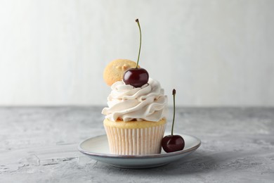 Photo of Delicious cupcake with cherries and cookie on grey textured table, closeup