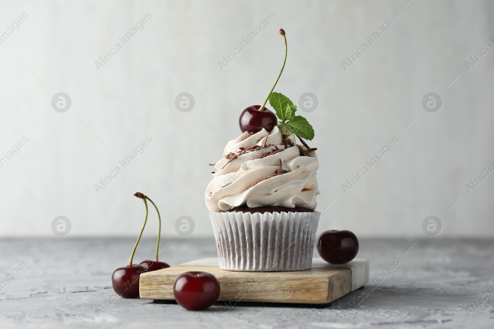 Photo of Delicious cupcake with cream and cherries on grey textured table