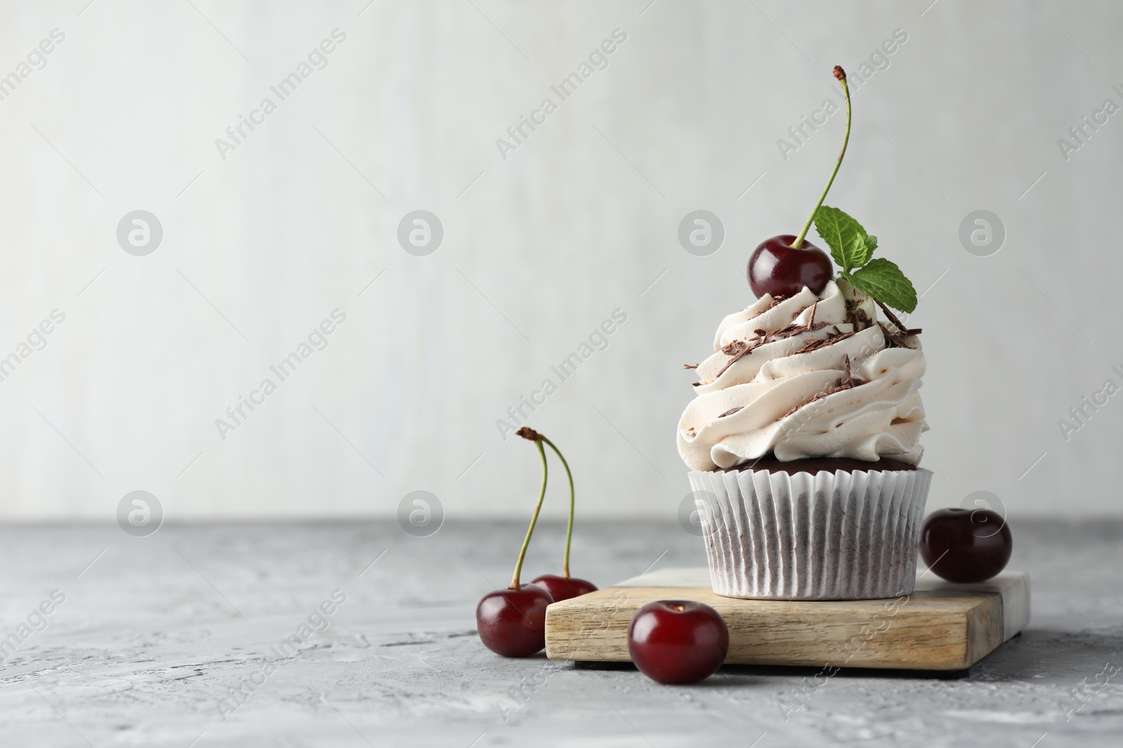 Photo of Delicious cupcake with cream and cherries on grey textured table, space for text