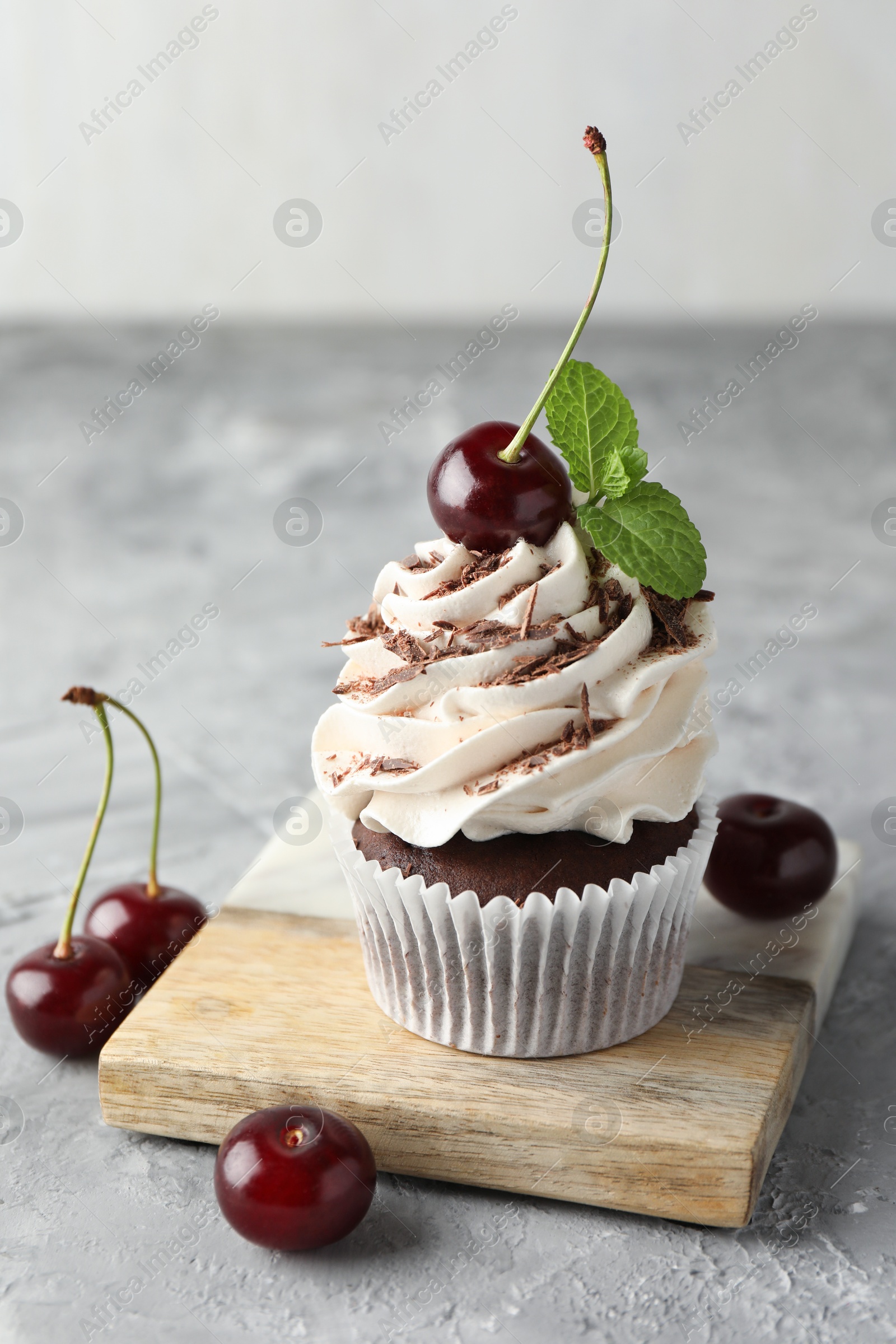 Photo of Delicious cupcake with cream and cherries on grey textured table