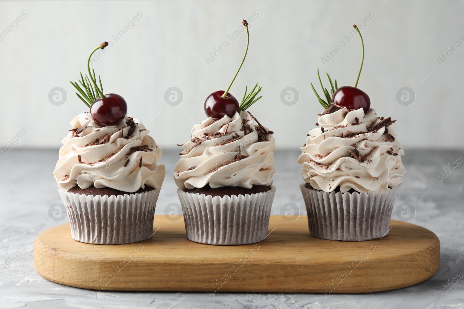 Photo of Delicious cupcakes with cream and cherries on grey textured table