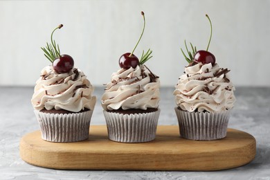 Photo of Delicious cupcakes with cream and cherries on grey textured table