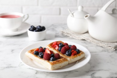 Photo of Tasty puff pastries with berries and tea on white marble table