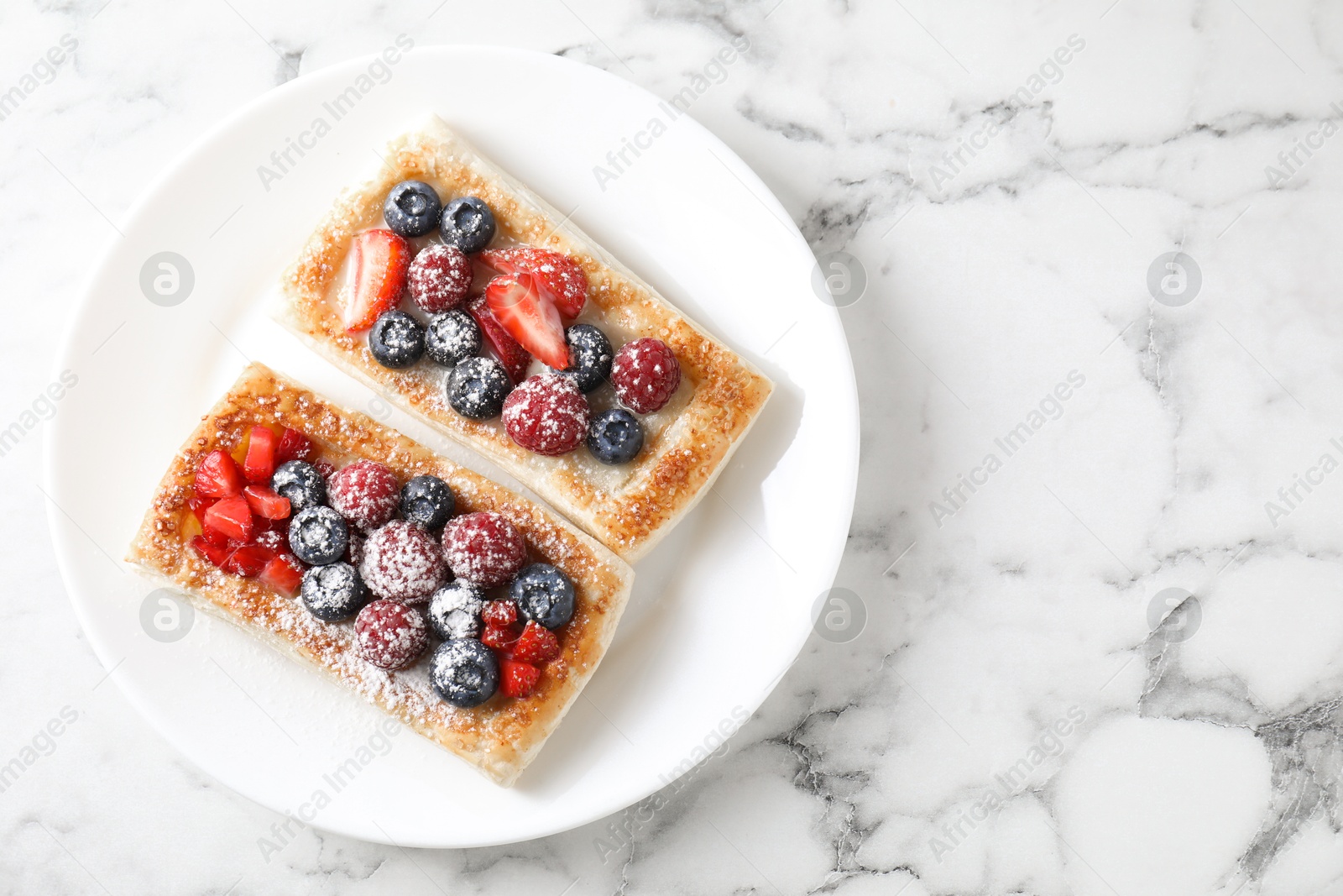 Photo of Tasty puff pastries with berries on white marble table, top view. Space for text