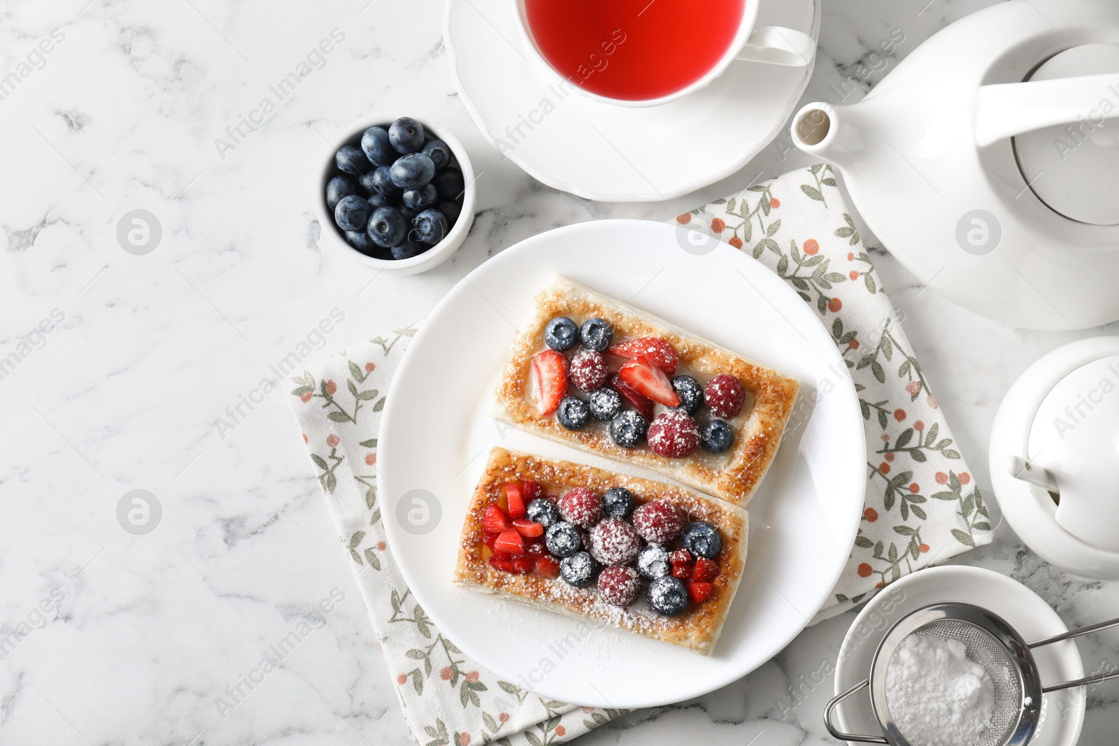 Photo of Tasty puff pastries with berries and tea on white marble table, flat lay. Space for text