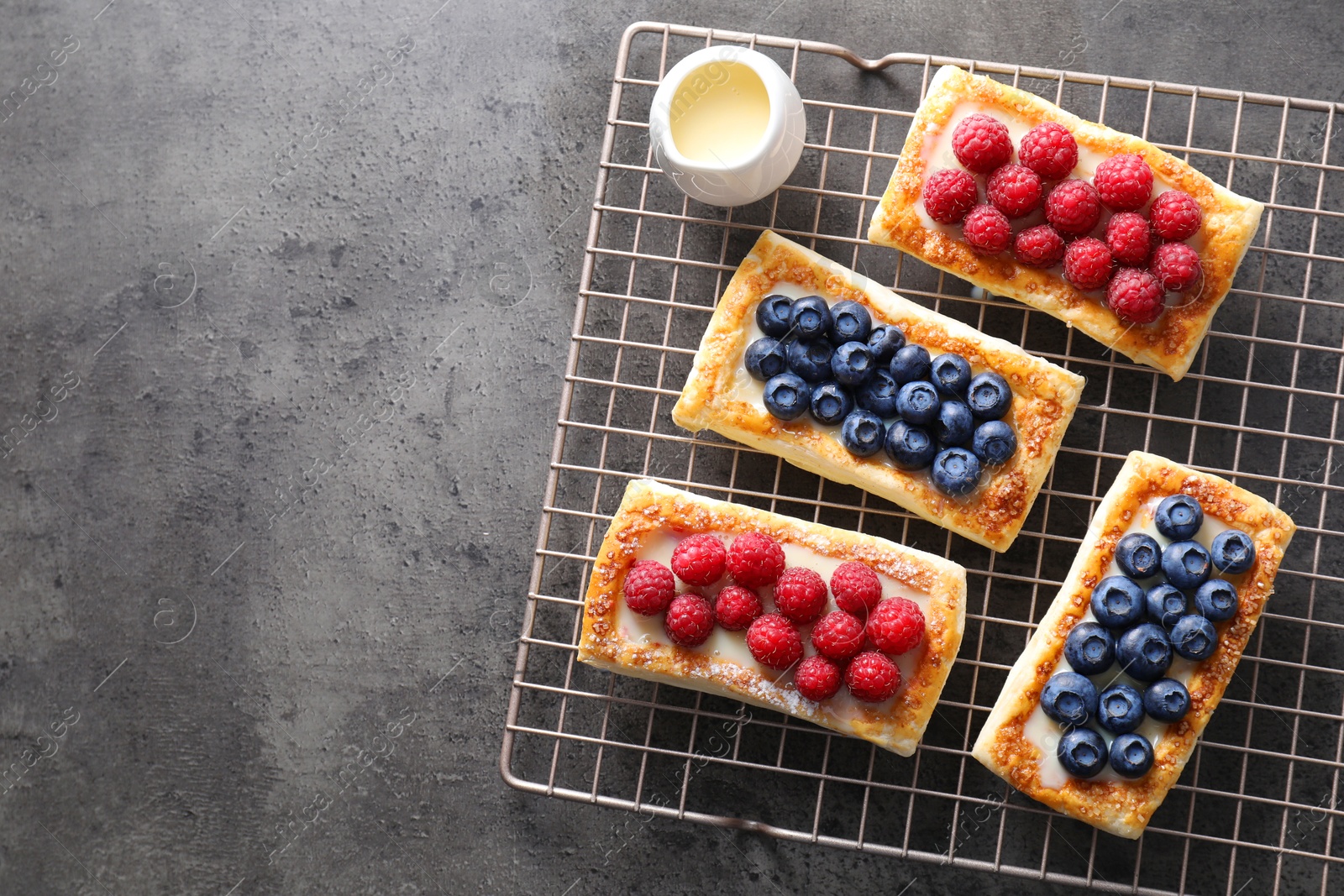 Photo of Tasty puff pastries with berries on grey table, top view. Space for text