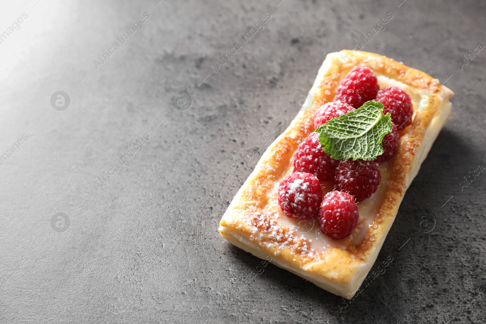 Photo of Tasty puff pastry with raspberries and mint on grey table, space for text