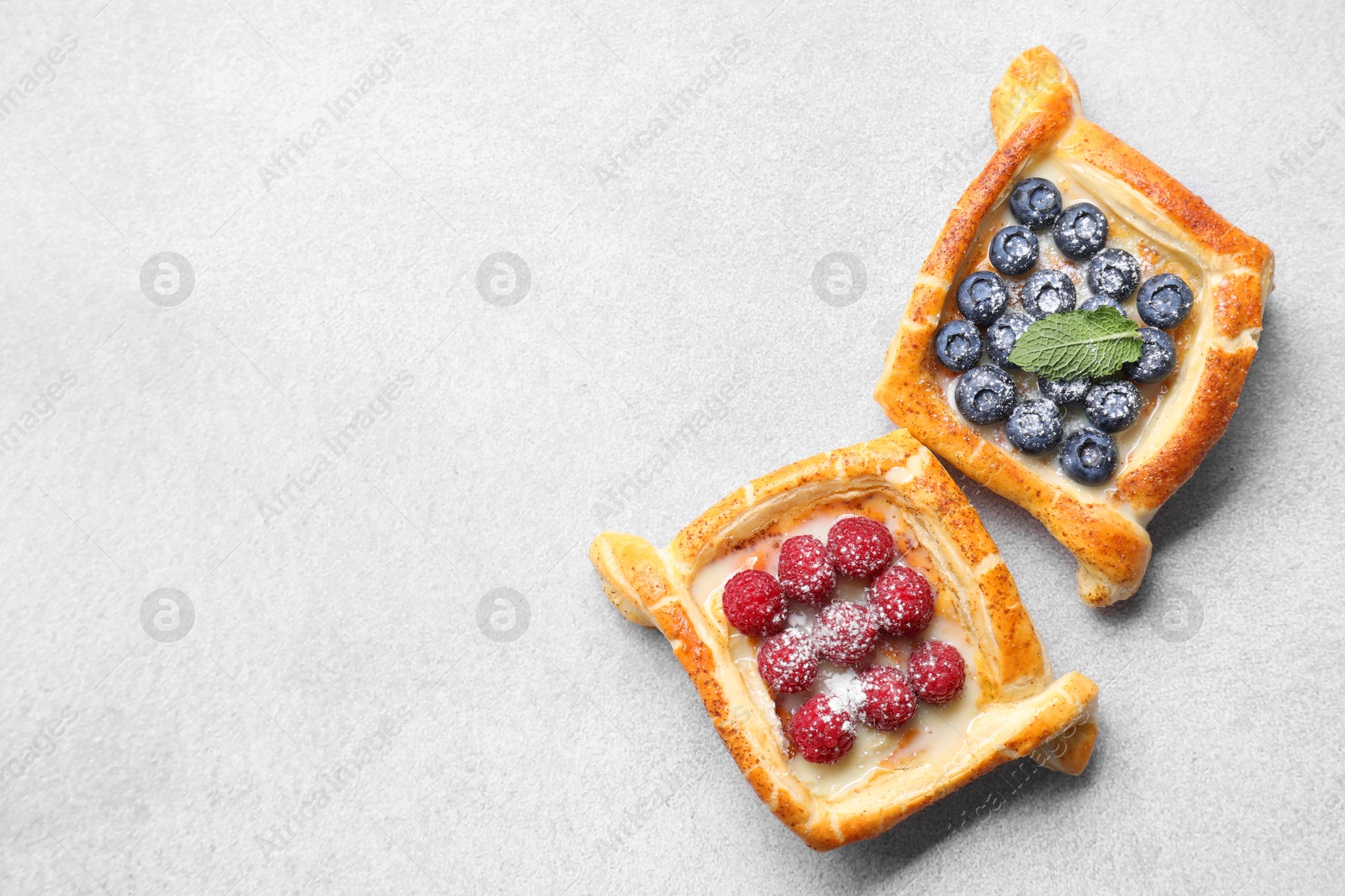 Photo of Tasty puff pastries with berries on white table, top view. Space for text