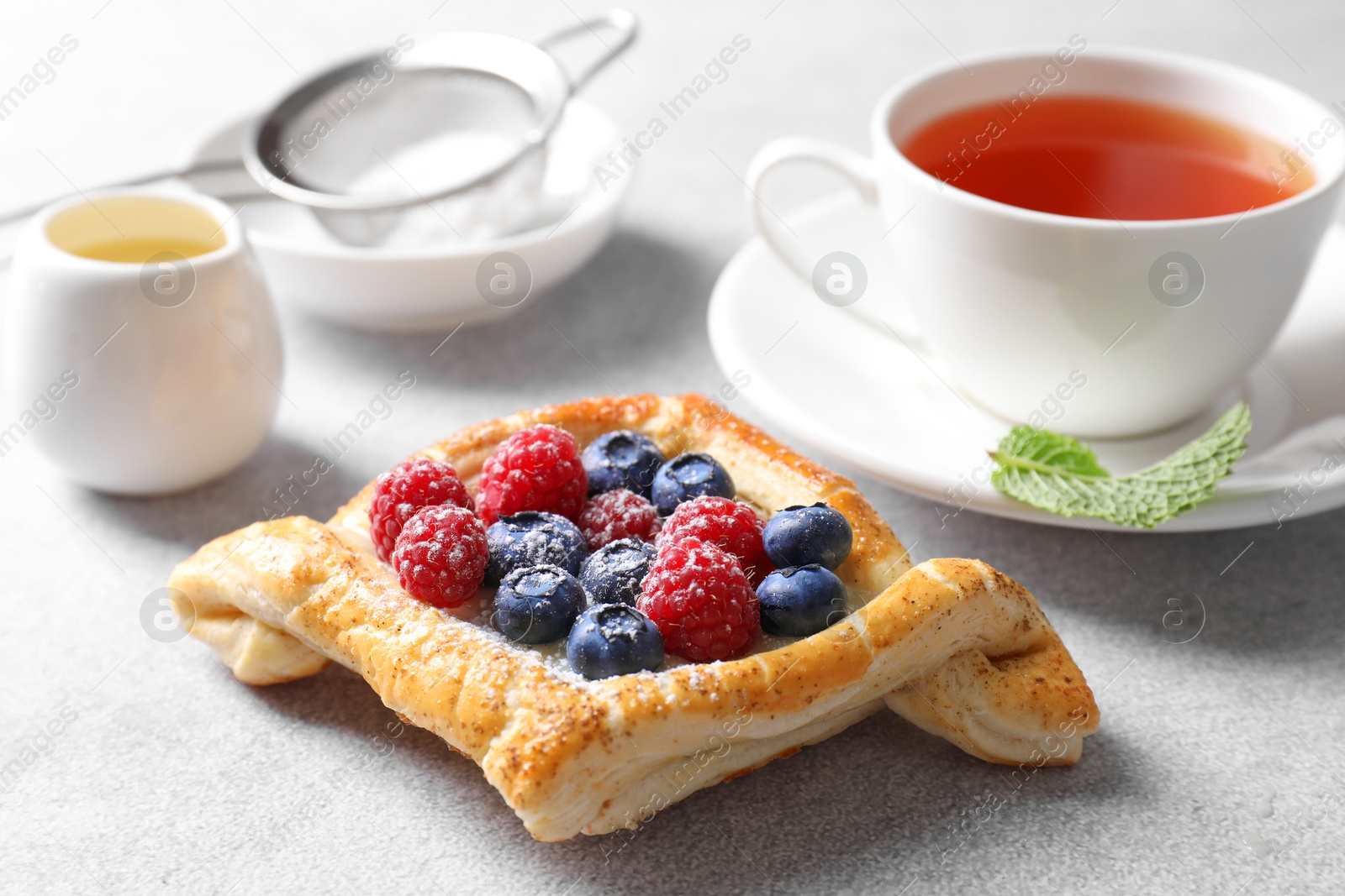 Photo of Tasty puff pastry with berries and tea on white table, closeup