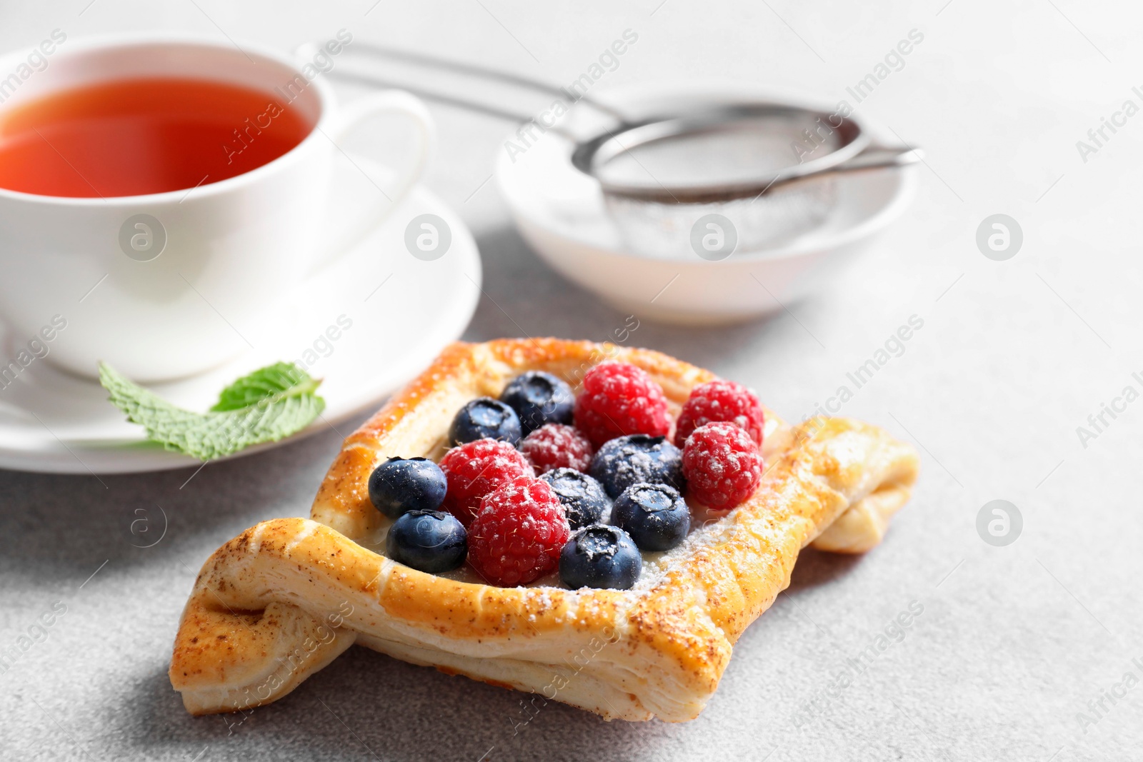 Photo of Tasty puff pastry with berries and tea on white table, closeup