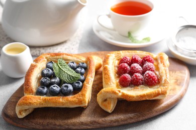 Photo of Tasty puff pastries with berries and tea on white table, closeup