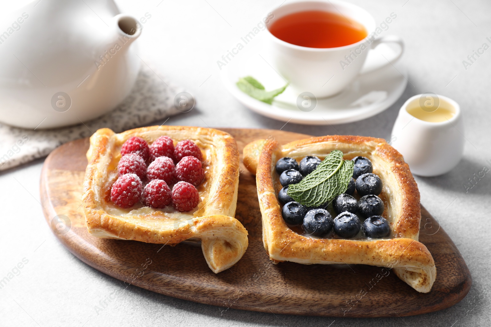 Photo of Tasty puff pastries with berries and tea on white table, closeup