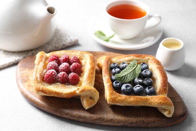 Photo of Tasty puff pastries with berries and tea on white table, closeup