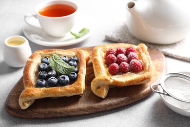 Photo of Tasty puff pastries with berries and tea on white table, closeup