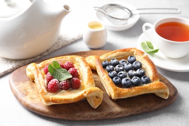 Tasty puff pastries with berries and tea on white table, closeup