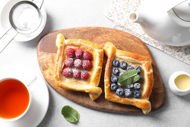 Photo of Tasty puff pastries with berries and tea on white table, flat lay