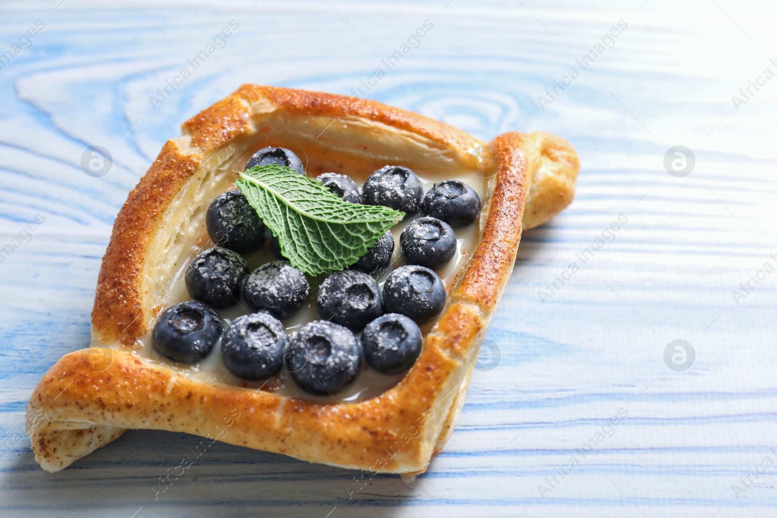 Photo of Tasty puff pastry with blueberries and mint on light blue wooden table, closeup. Space for text