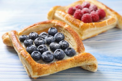 Tasty puff pastries with berries on light blue wooden table, closeup