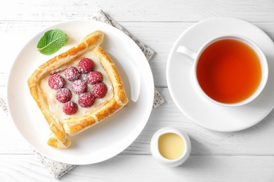 Photo of Tasty puff pastry with raspberries and tea on white wooden table, flat lay