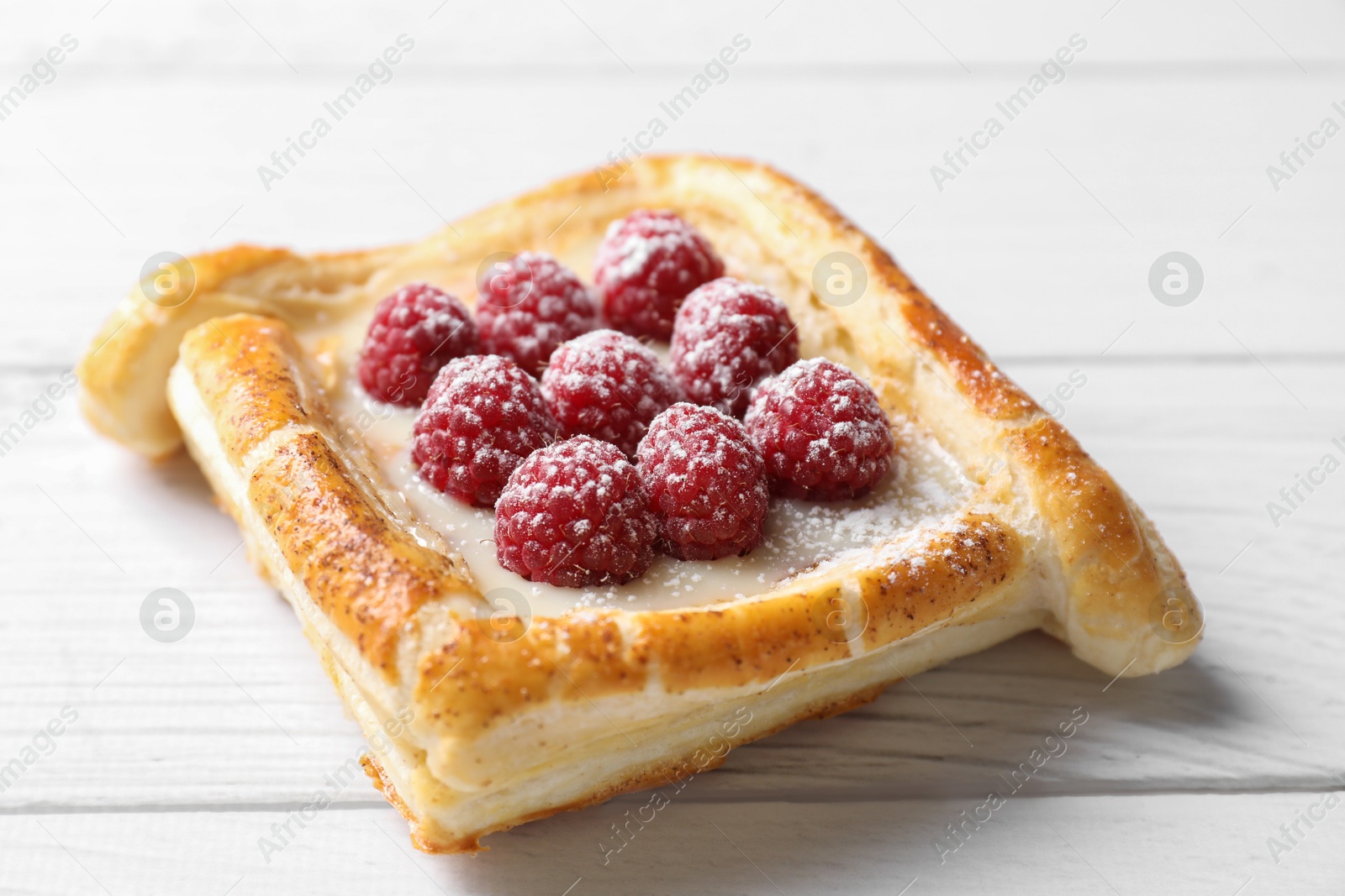 Photo of Tasty puff pastry with raspberries on white wooden table, closeup