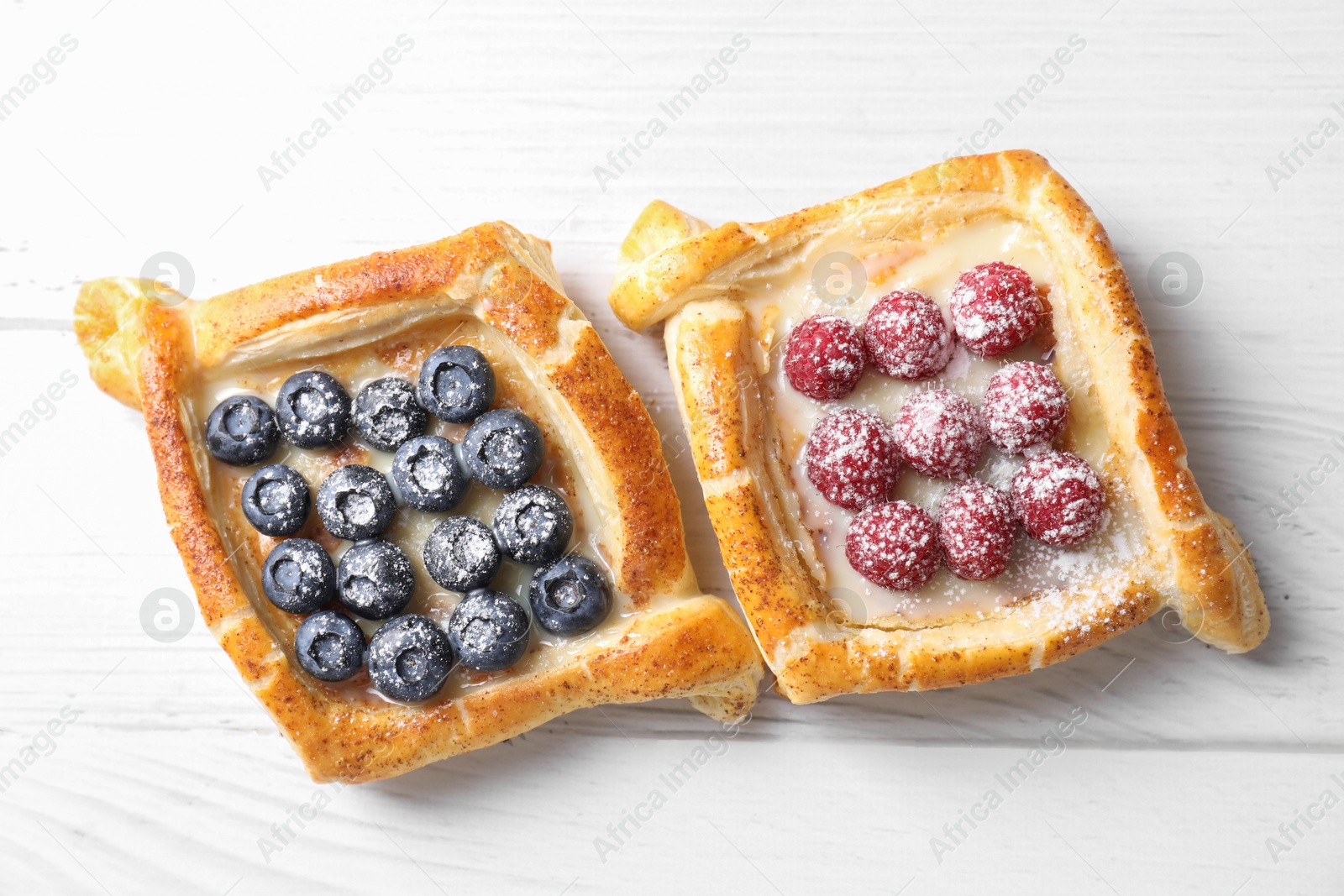 Photo of Tasty puff pastries with berries on white wooden table, top view