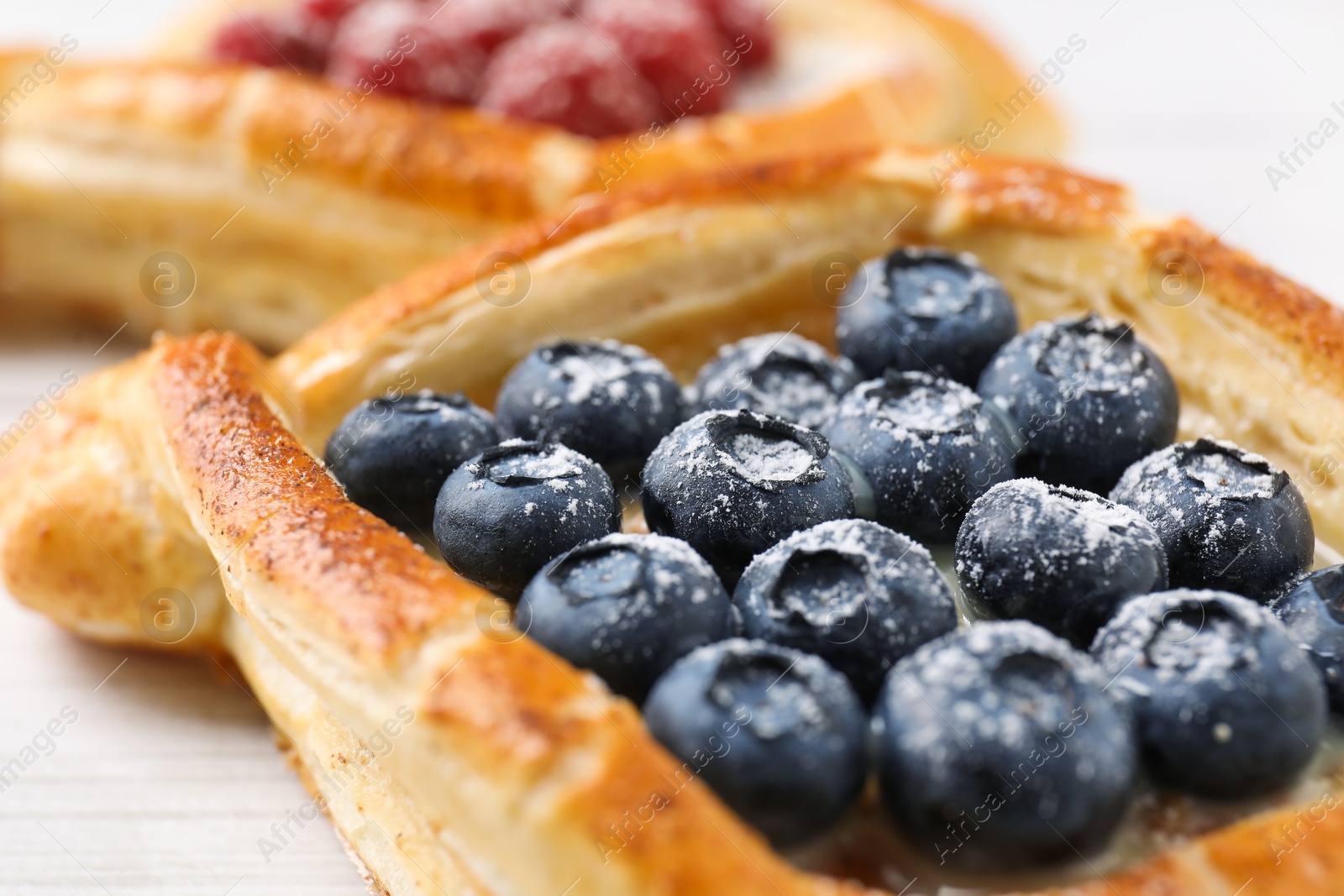 Photo of Tasty puff pastries with berries on white wooden table, closeup