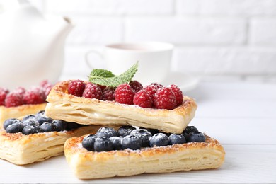 Photo of Tasty puff pastries with berries on white wooden table, closeup