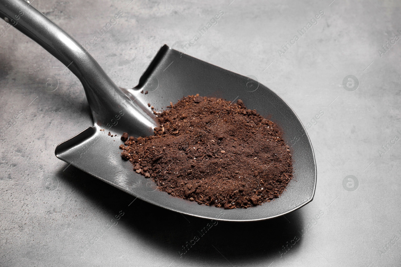 Photo of Metal shovel with soil on grey table