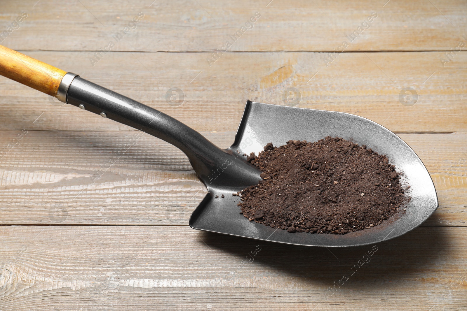 Photo of Metal shovel with soil on light wooden table