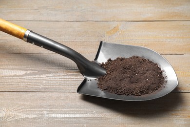 Photo of Metal shovel with soil on light wooden table