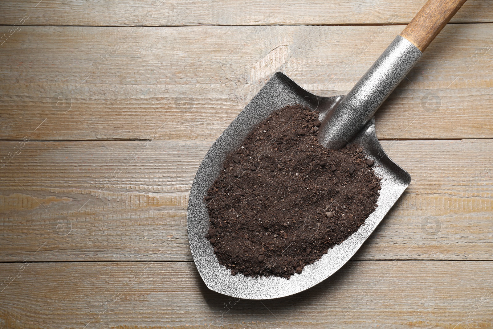 Photo of Metal shovel with soil on light wooden table, top view. Space for text