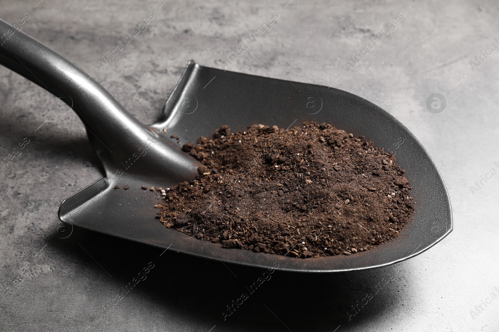 Photo of Metal shovel with soil on grey table, closeup