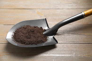 Photo of Metal shovel with soil on wooden table