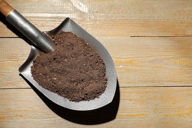 Photo of Metal shovel with soil on wooden table, top view. Space for text