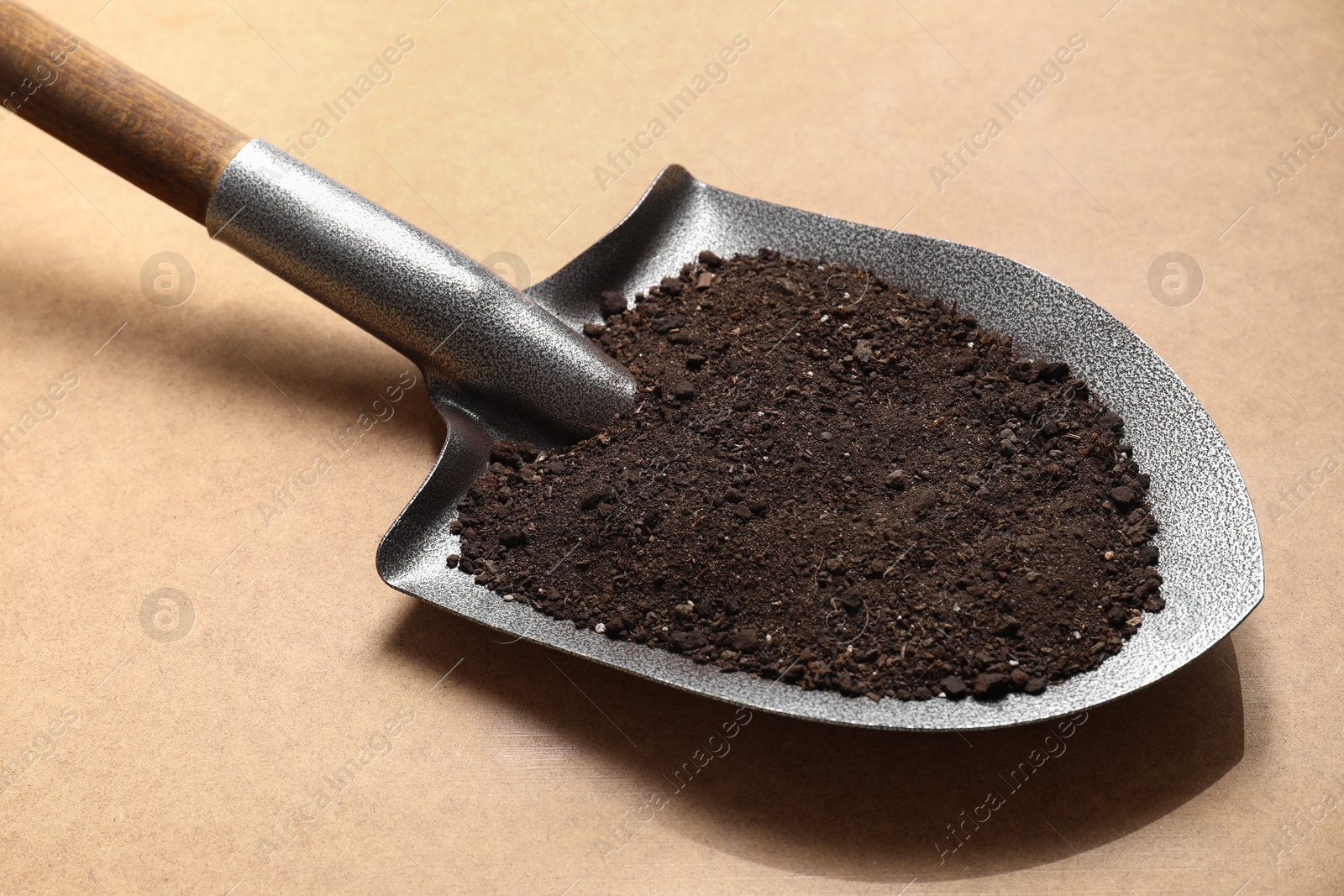 Photo of Metal shovel with soil on light brown table