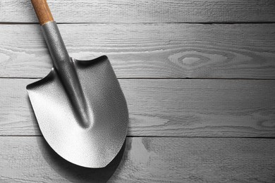 Photo of Metal shovel on light grey wooden table, top view. Space for text