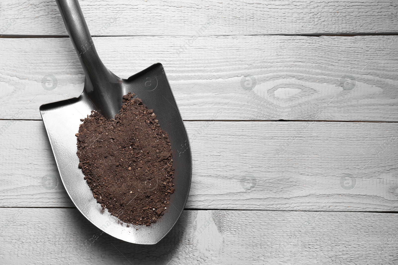 Photo of Metal shovel with soil on light grey wooden table, top view. Space for text