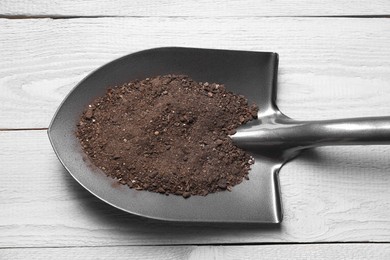 Photo of Metal shovel with soil on light grey wooden table, top view