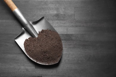 Photo of Metal shovel with soil on black wooden table, top view. Space for text