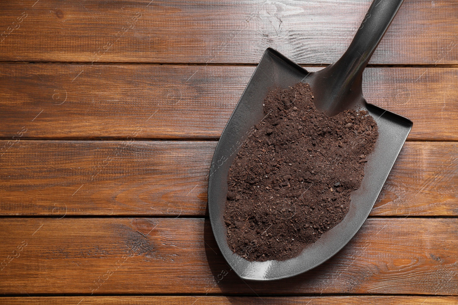 Photo of Metal shovel with soil on wooden table, top view. Space for text