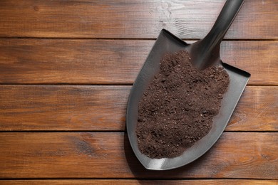 Photo of Metal shovel with soil on wooden table, top view. Space for text