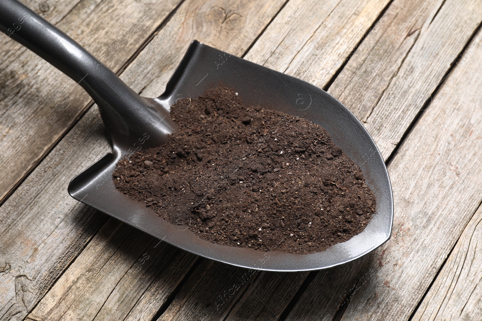 Photo of Metal shovel with soil on wooden table, closeup