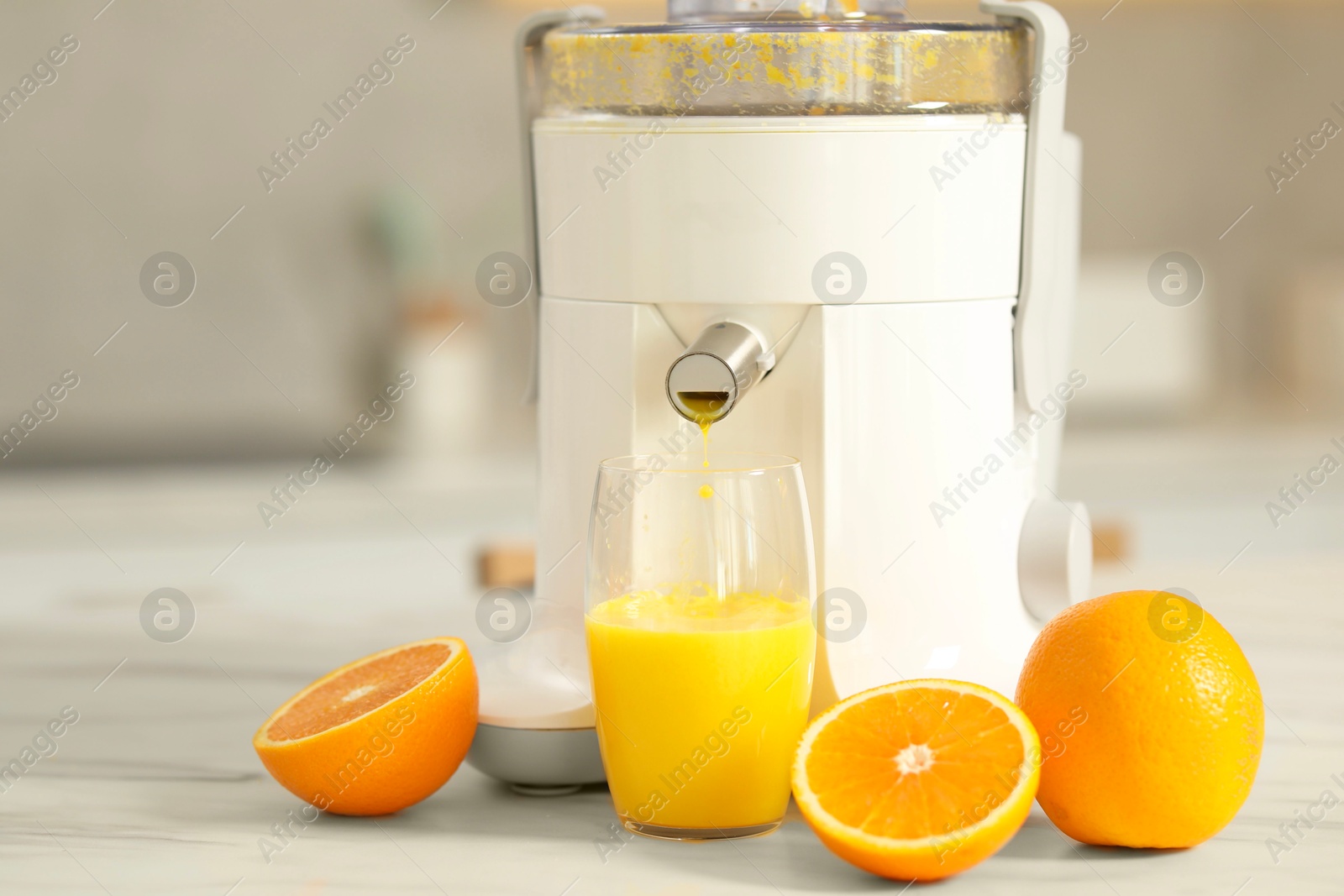 Photo of Modern juicer, oranges and glass on white marble table in kitchen