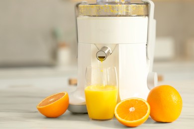 Photo of Modern juicer, oranges and glass on white marble table in kitchen