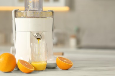 Photo of Modern juicer, oranges and glass on white marble table in kitchen, space for text